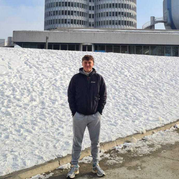 A happy, smiling student wearing a navy top, standing in front of a building.