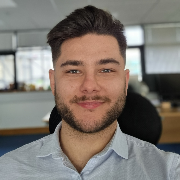 A happy smiling degree apprentice with his office in the background.