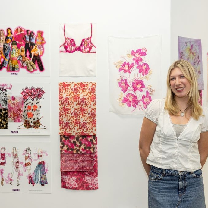 A happy smiling student standing proudly in front of her colourful work.