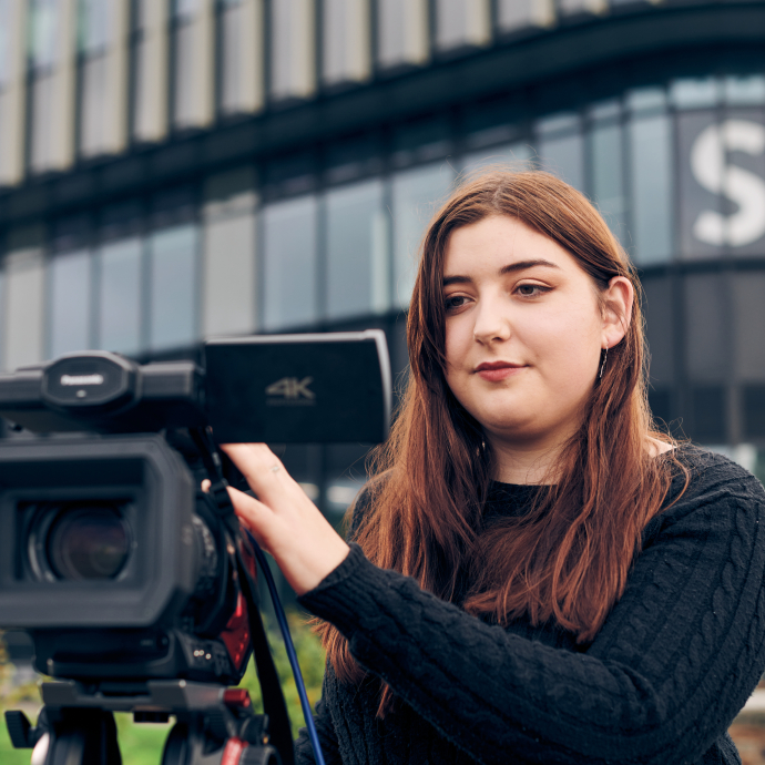 woman standing behind camera in front of building that says S4C