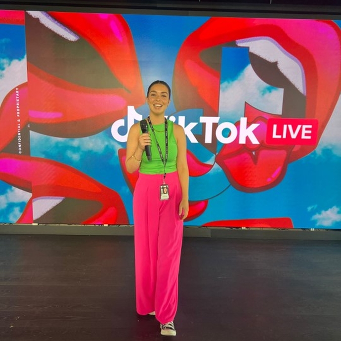 woman holding a microphone in front of backdrop that's branded 'TikTok Live'