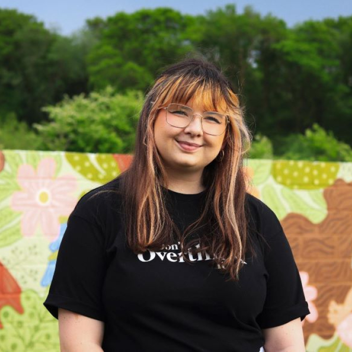 A smiling student dressed in a black t-shirt, standing in front of a brightly-coloured mural.