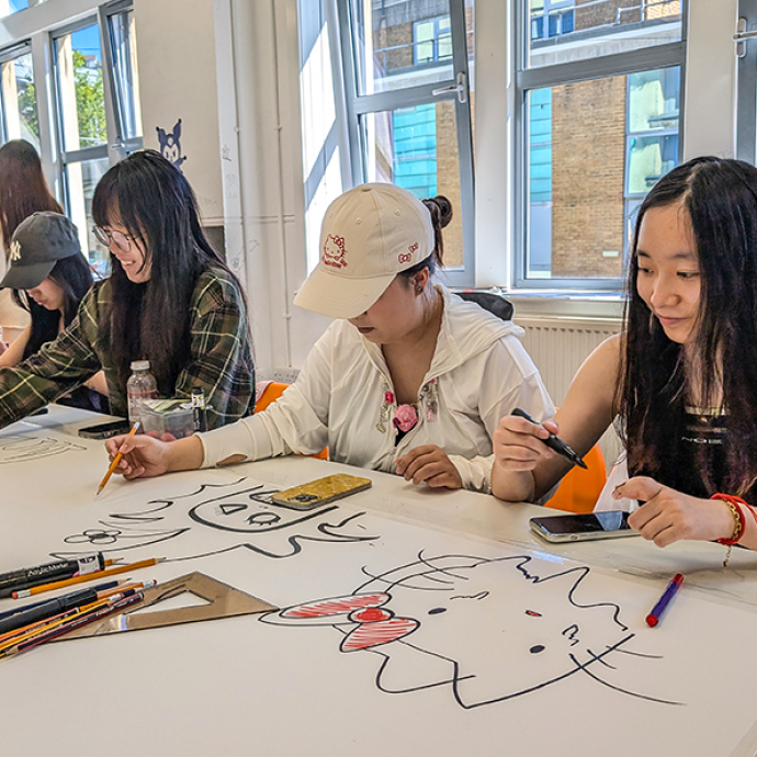 Students sitting at a large white desk using their creative skills.