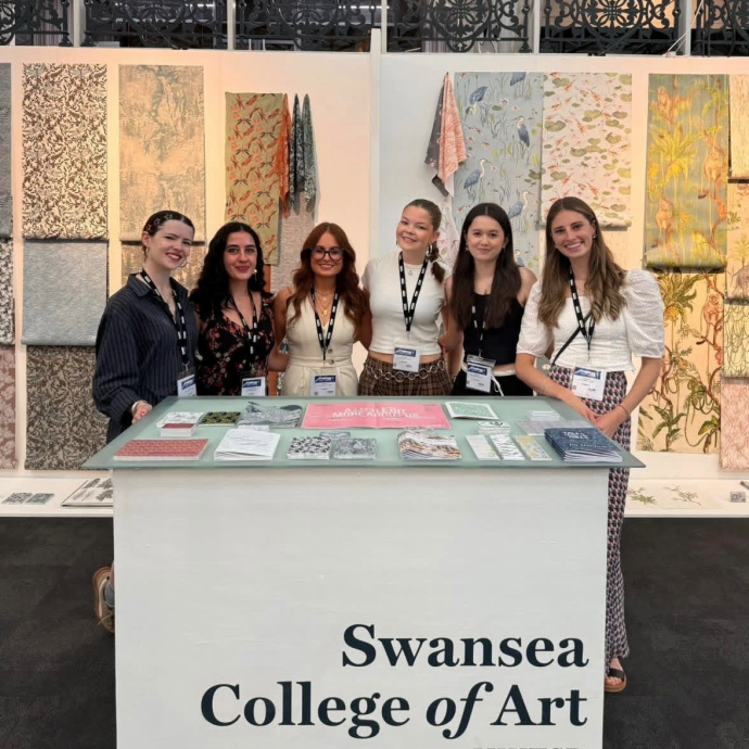 Six smiling, happy and proud students pictured against a colourful backdrop of their creative work.