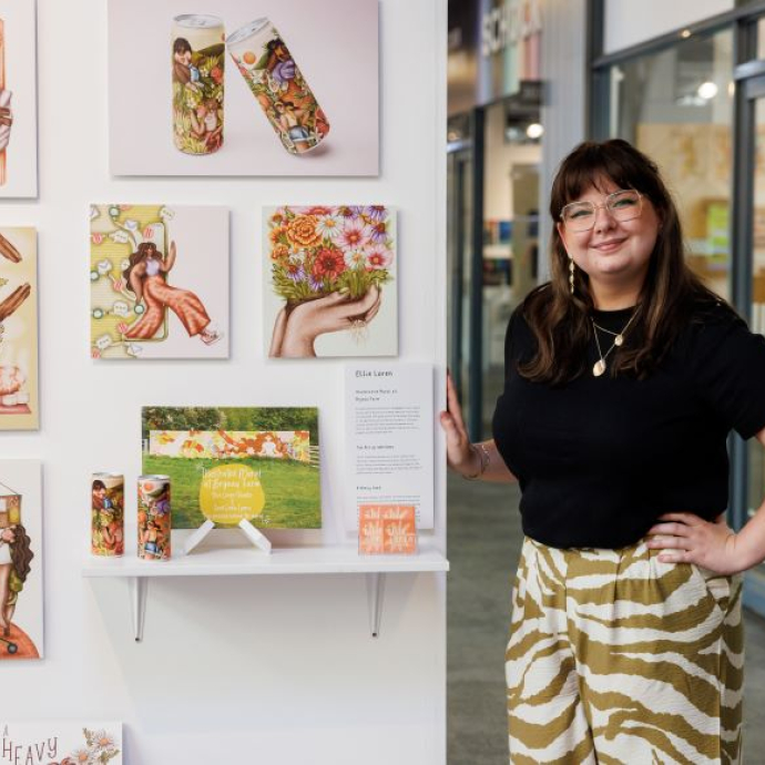 A smiling graduate standing proudly by her amazing creative work.