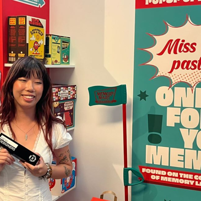 A smiling student in a white top holding an award and standing in front of her creative work.