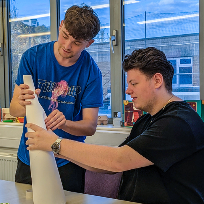 Two students, one seated and the other standing concentrating on a creative task.