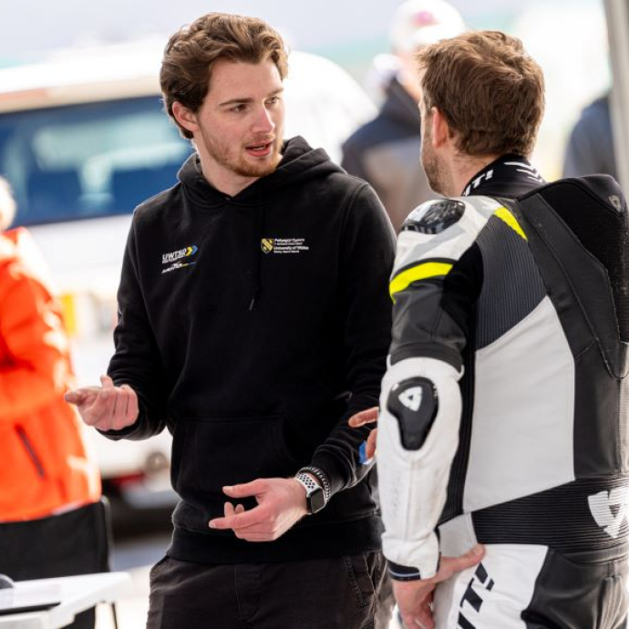 Two students in branded clothing talking against a racing background.