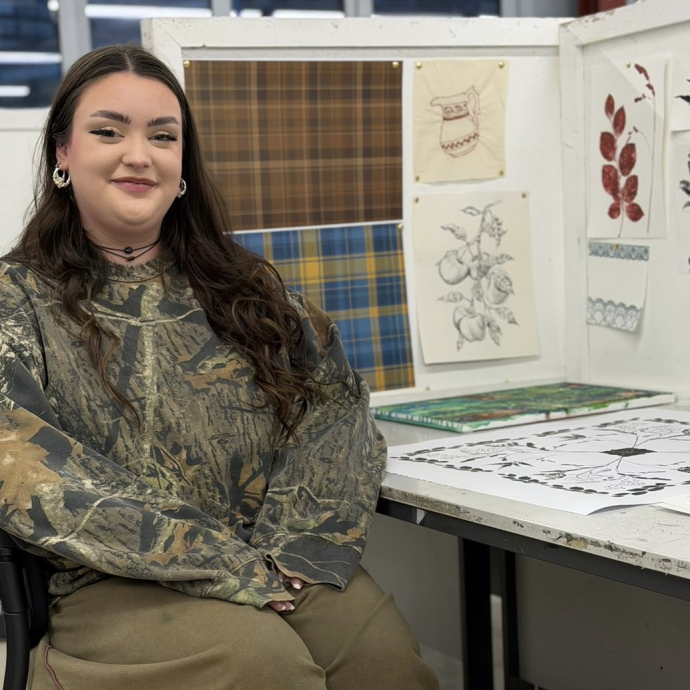 A student sitting at her desk in a workshop with creative work on show.