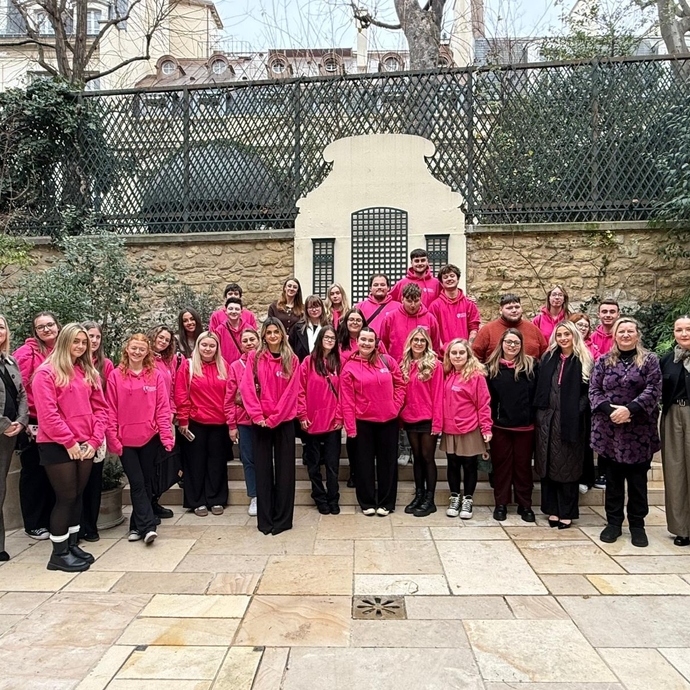 A large group of students and lecturers in branded bright pink hoodies, standing outside in front of a conference building.