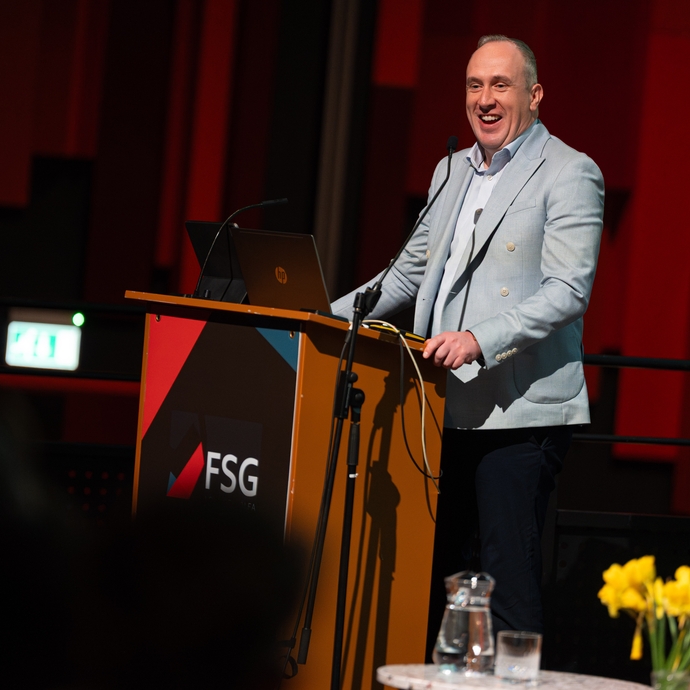 A man standing behind a podium and microphone on a stage, smiling