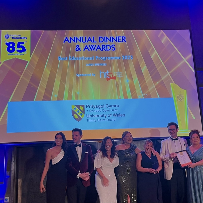 A group of staff and students in evening dress celebrating against a branded background.