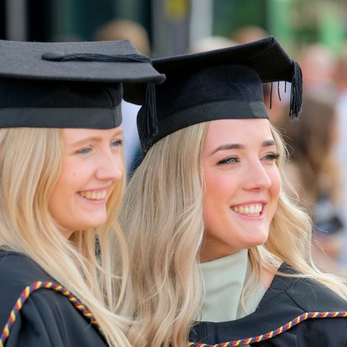 Two graduates in their caps and gowns smiling and posing for a photograph.