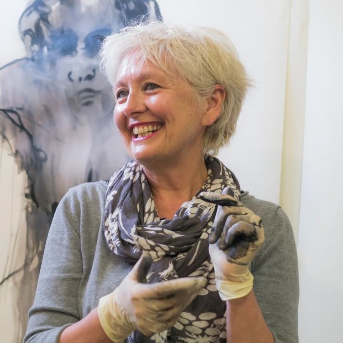 A smiling lady wearing craft gloves wearing a scarf.