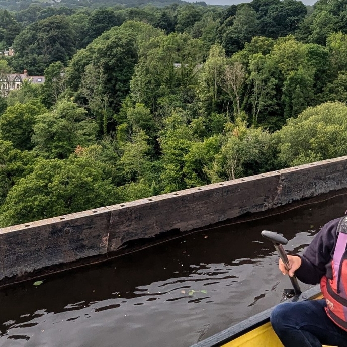 A person in a canoe on high bridge with trees and river down below in background 