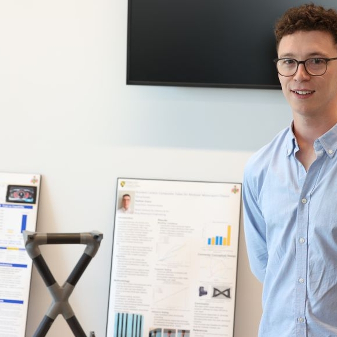 A student dressed in a smart blue shirt standing proudly by his work.