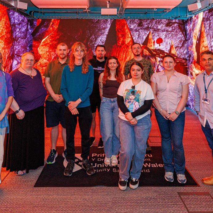 Group photo fo students with Dr Rebekah Humphreys and Dt Nik Whitehead in the immersive room with visuals on screens