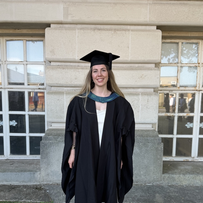 A woman standing in front of building in gap and gown on graduation day