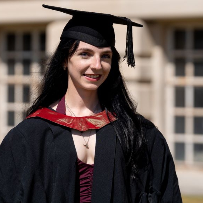 A smiling and proud graduate standing in her cap and gown.