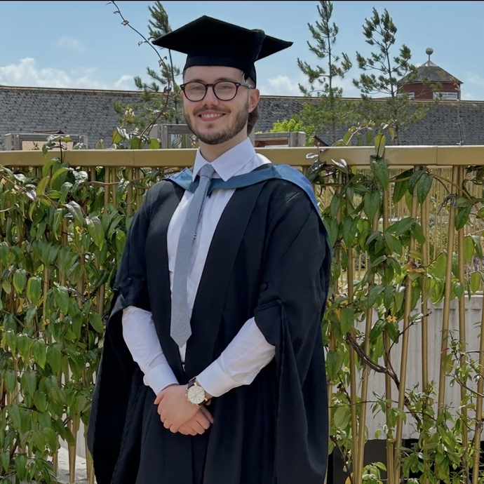 A proud and smiling graduate dressed in cap and gown with his arms folded in front.