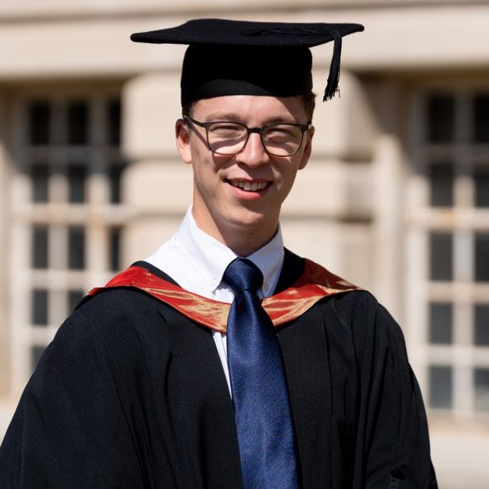 A smiling and proud graduate standing in his cap and gown.