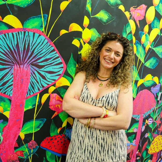 A smiling graduate standing with her arms folded in front of a vibrant mural.