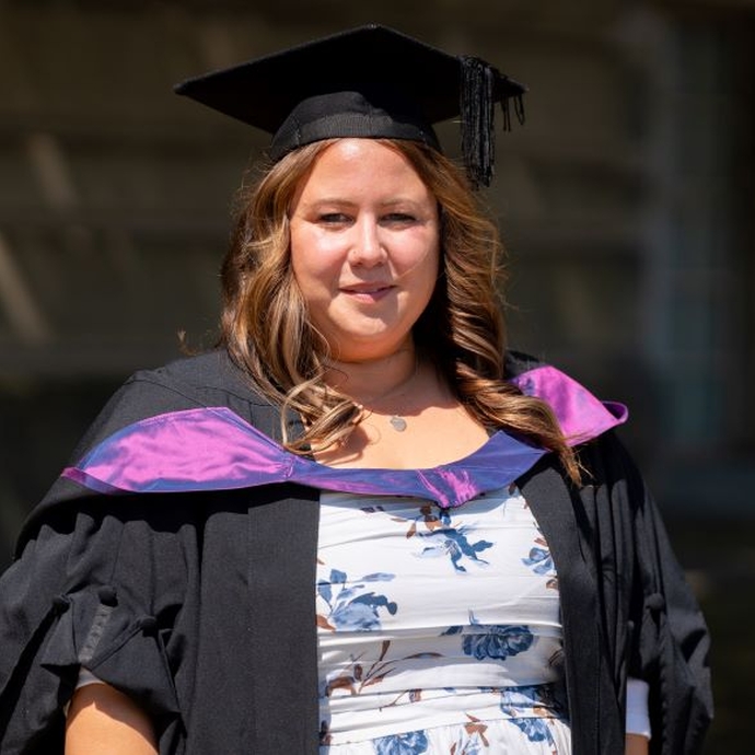 A smiling and proud graduate standing in her cap and gown.