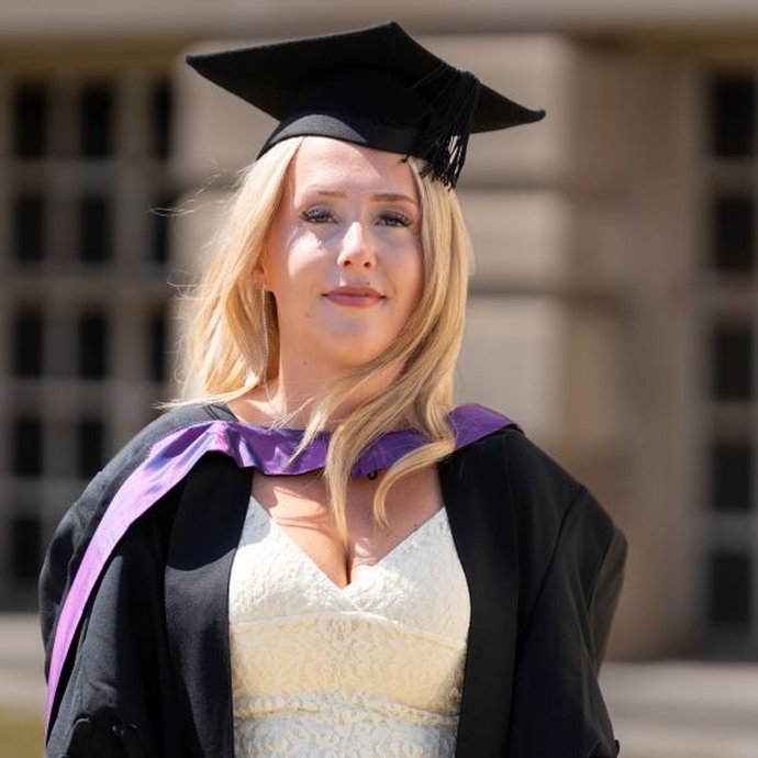 A smiling and proud graduate standing in her cap and gown.