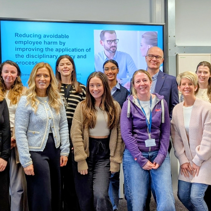 A group of people stood in front of large digital screen posing for a group photo