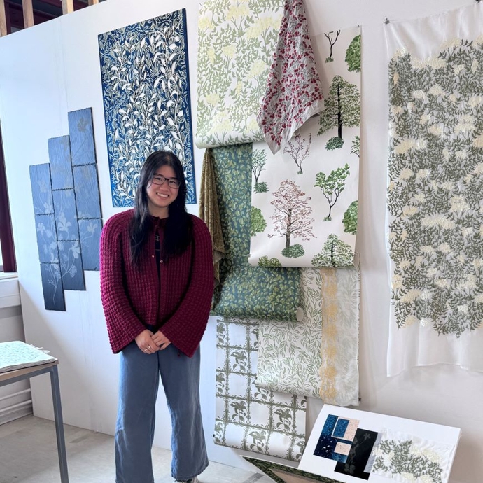 A student standing proudly in front of vibrant art work on a white wall.