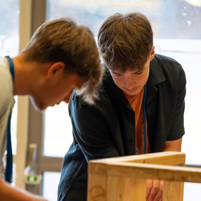 Two students working on a wooden structure.