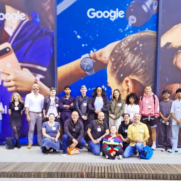 A large group of students, some seated and standing against a vibrant blue branded background.